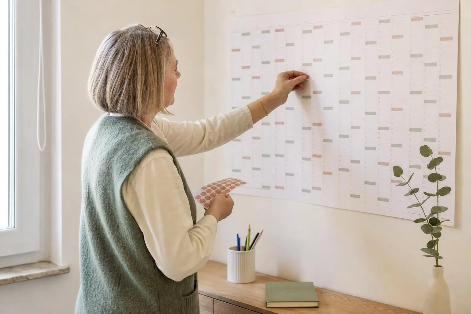 Sage-femme d’une cinquantaine d’années debout devant un grand calendrier mural en papier, posant des pastilles de couleur sur des semaines